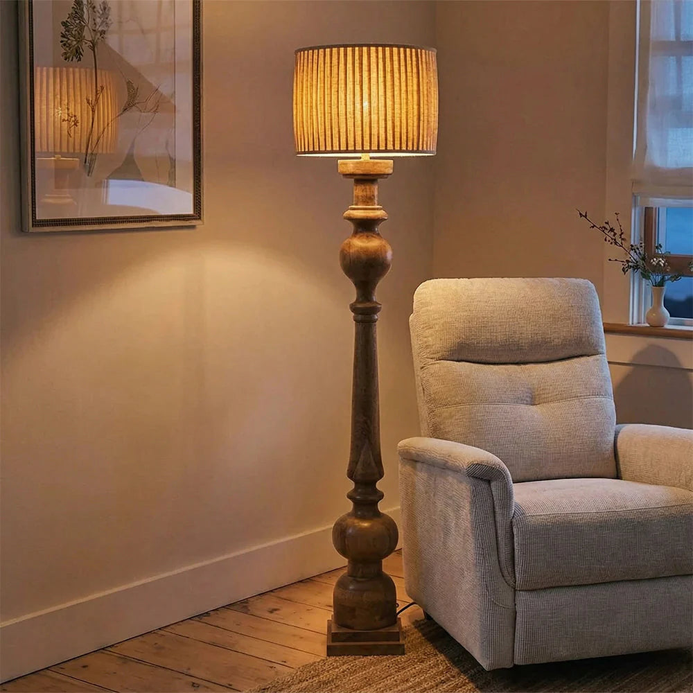 Floor lamp with a beige shade next to a gray armchair in a room with wooden flooring.