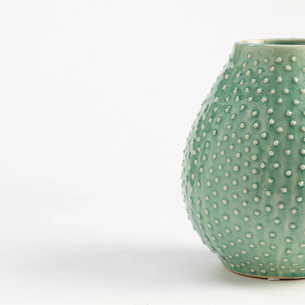 Green ceramic vase with white dot pattern on a white background