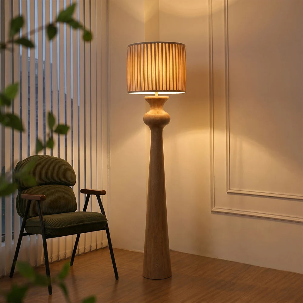 Tall floor lamp with a wooden base and beige shade in a room with a chair and plants.