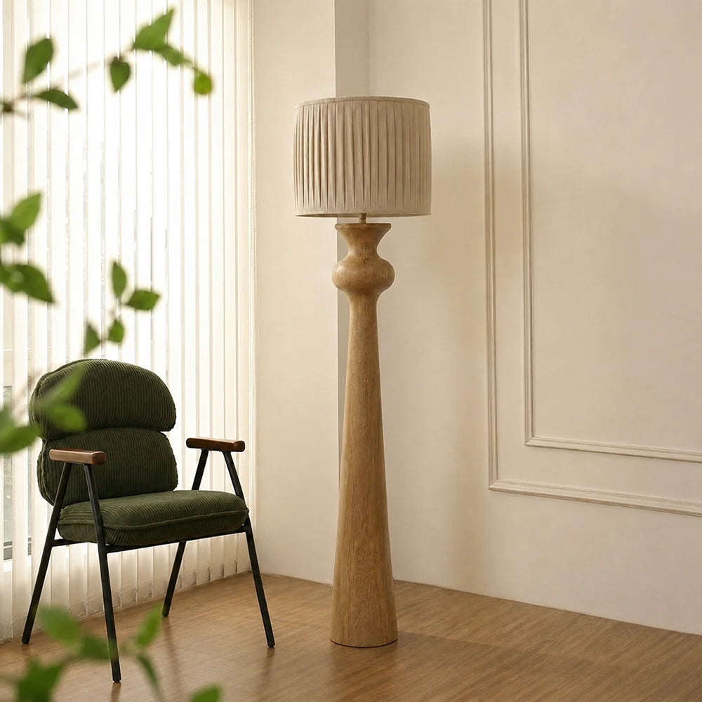 Tall floor lamp with a textured shade next to a green armchair in a room with light-colored walls and wooden flooring.
