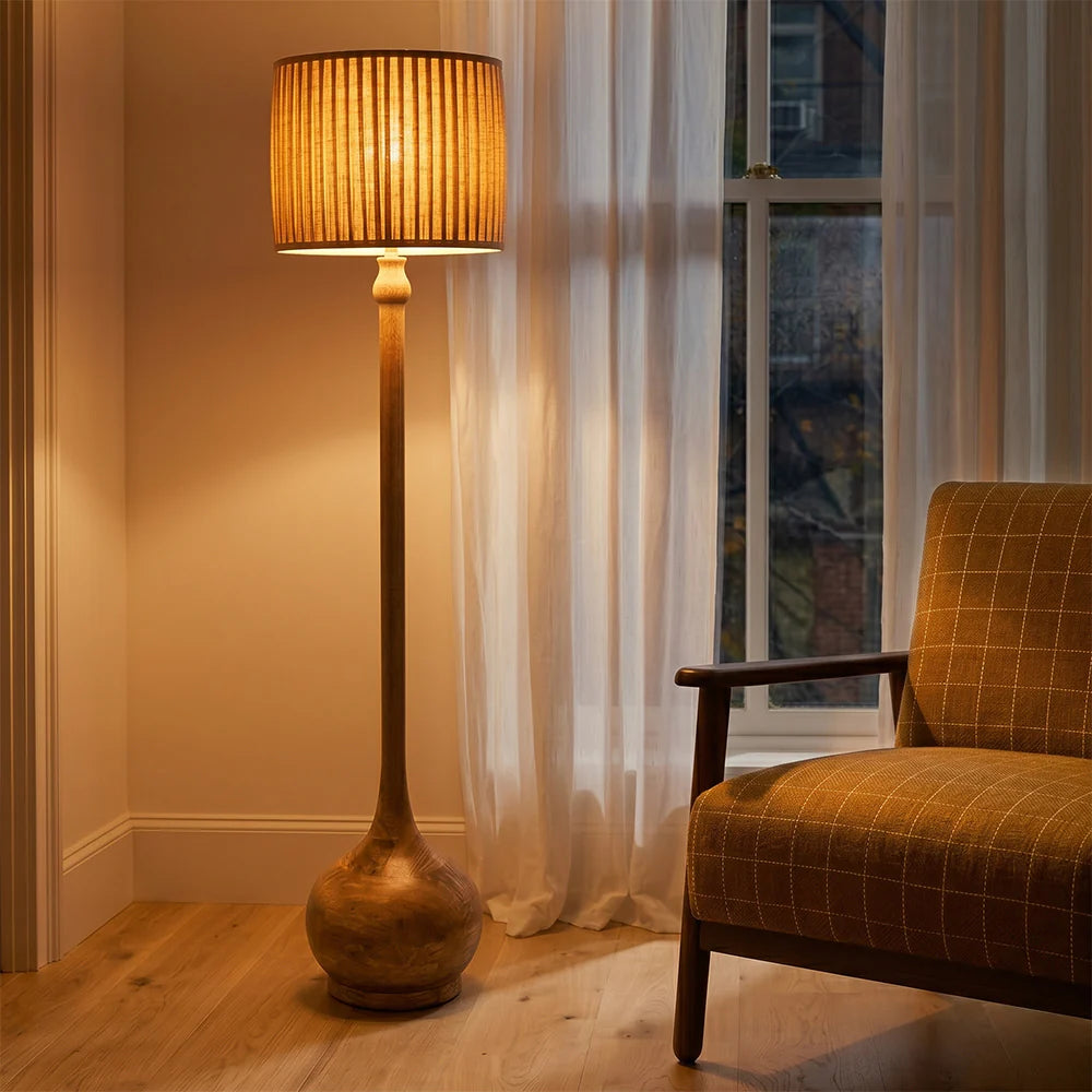 Floor lamp with a textured shade next to a chair in a room with a window and curtains.