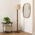 Wooden floor lamp with a beige shade in a room with a side table and mirror.