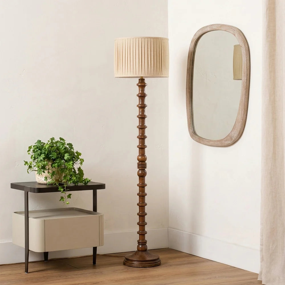 Wooden floor lamp with a beige shade in a room with a side table and mirror.